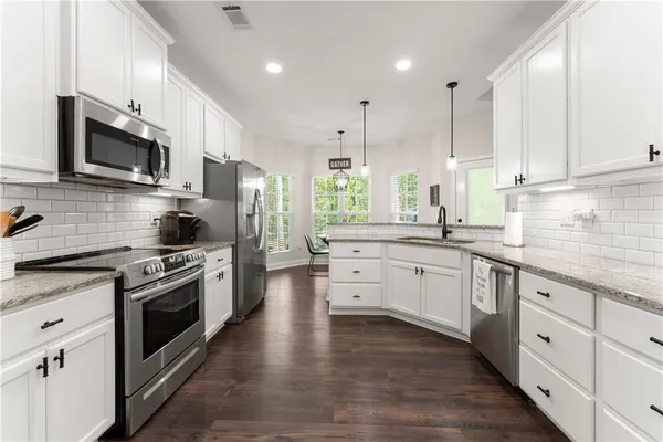 a kitchen with stainless steel appliances kitchen island granite countertop a stove a sink and white cabinets