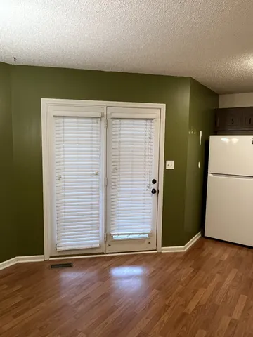 an empty room with wooden floor and a refrigerator