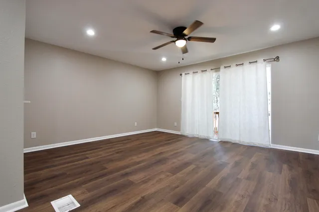 a view of an empty room with wooden floor and a window