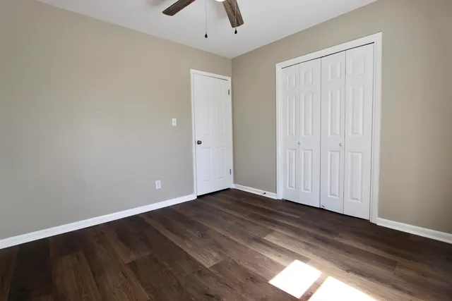 an empty room with wooden floor chandelier fan and windows