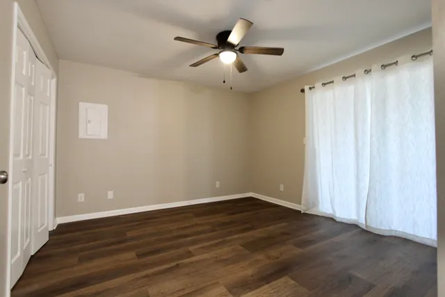an empty room with wooden floor fan and windows
