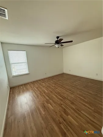 an empty room with wooden floor fan and windows