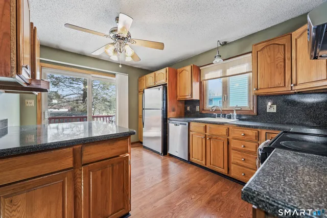 a kitchen with stainless steel appliances granite countertop a refrigerator a sink dishwasher a stove and white countertops with wooden floor