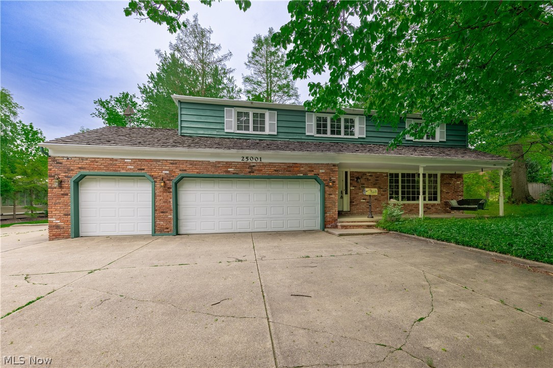 25001 Letchworth Road Beachwood, OH 44122 - Photo 1 of 50 Brick and siding exterior featuring a two-car garage with panel doors, a covered front porch, and dormer windows with shutters
