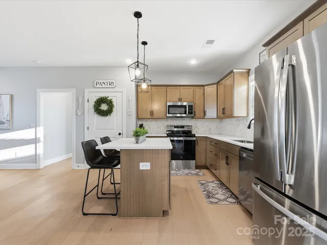a kitchen with stainless steel appliances kitchen island granite countertop a refrigerator a stove a sink dishwasher and white cabinets with wooden floor