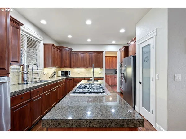 a kitchen with stainless steel appliances granite countertop a refrigerator a sink dishwasher a stove and white countertops with wooden floor