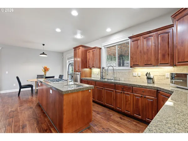 a kitchen with stainless steel appliances granite countertop wooden cabinets a stove a sink a dining table and chairs