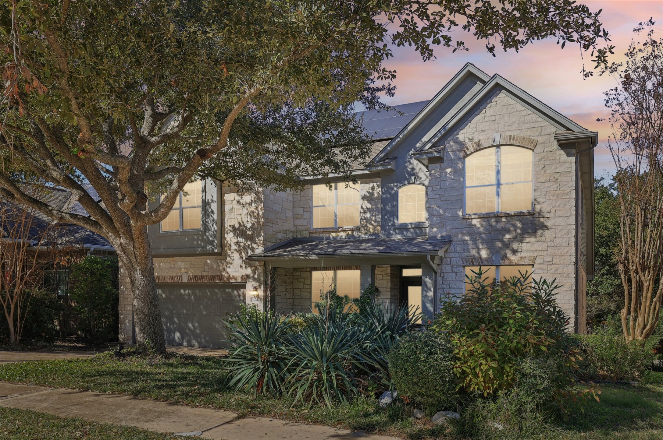 Traditional-style home featuring roof mounted solar panels, stone siding, a garage, and fence