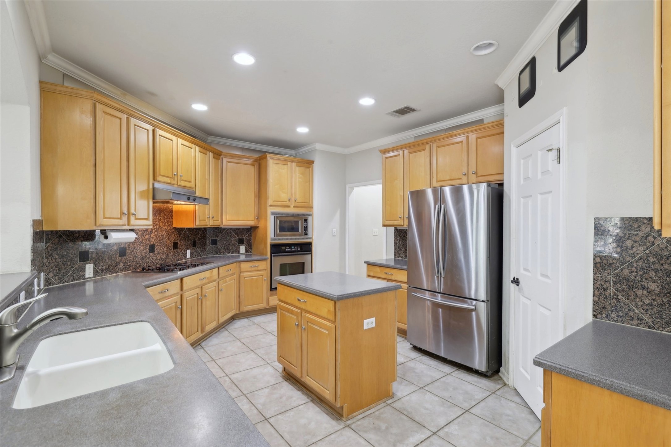 2948 Grimes Ranch Road Austin, TX 78732 - Photo 12 of 40 Kitchen featuring stainless steel appliances, a sink, under cabinet range hood, ornamental molding, and backsplash