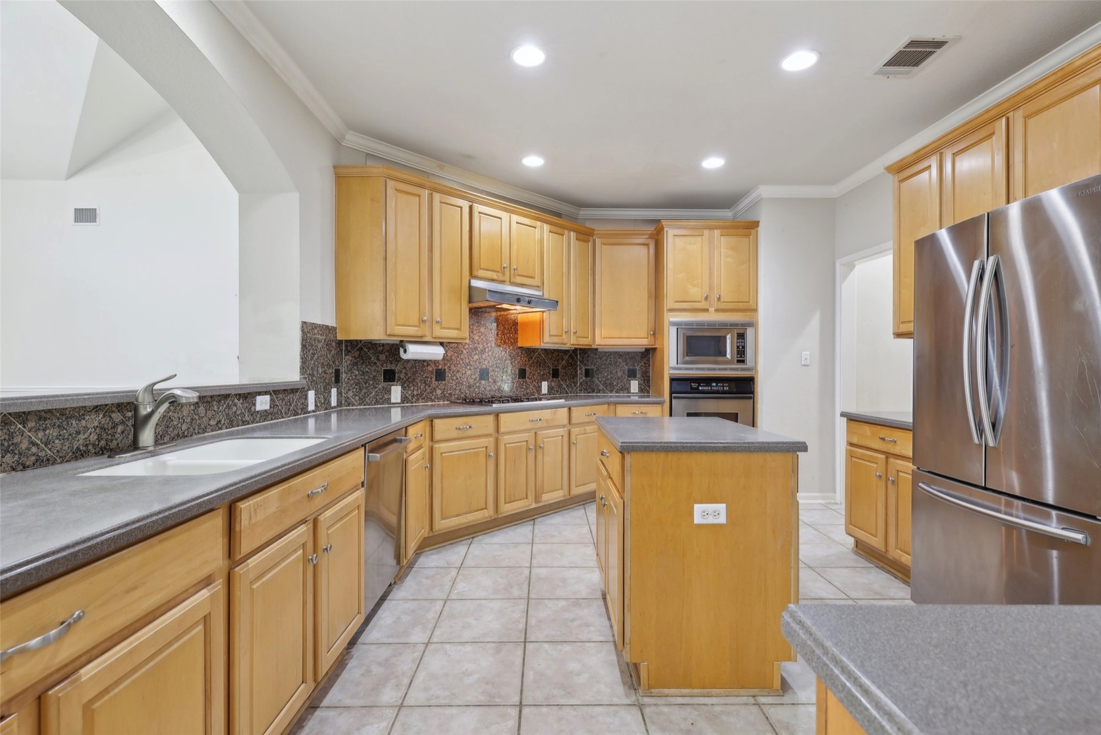 2948 Grimes Ranch Road Austin, TX 78732 - Photo 13 of 40 Kitchen featuring stainless steel appliances, a sink, under cabinet range hood, ornamental molding, and backsplash