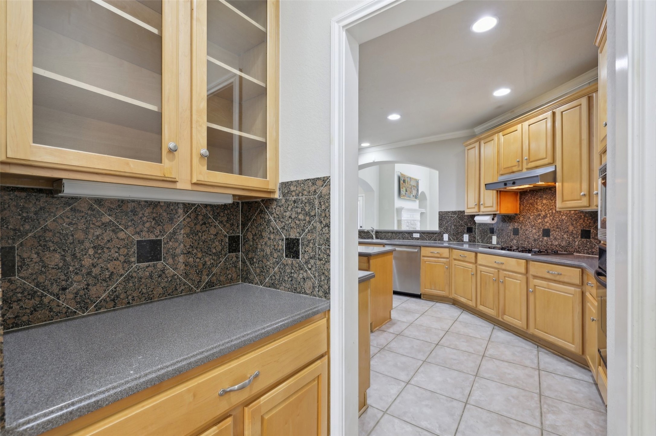 2948 Grimes Ranch Road Austin, TX 78732 - Photo 14 of 40 Kitchen prep area featuring light wood cabinetry with glass-front uppers, a dark speckled countertop, and a granite tile backsplash.
