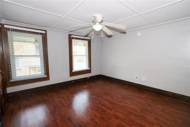 an empty room with wooden floor fan and windows