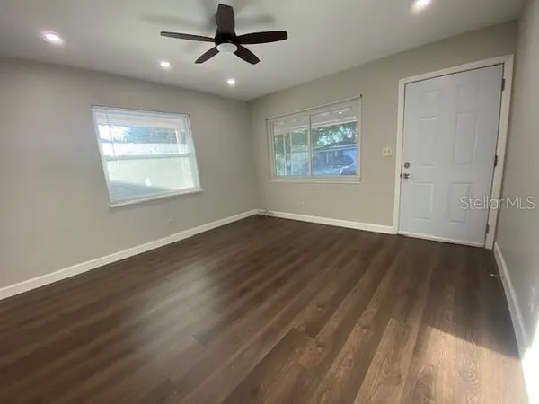 an empty room with wooden floor ceiling fan and windows