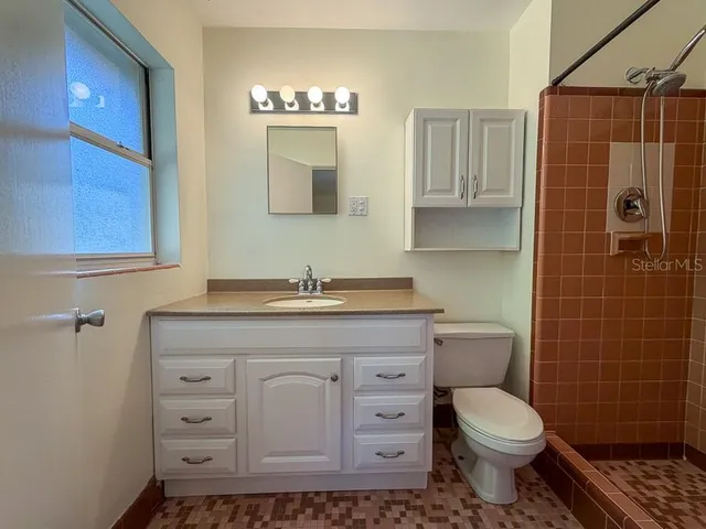 a bathroom with a granite countertop toilet a sink a mirror and shower