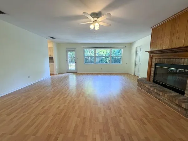 an empty room with windows fireplace and a kitchen view