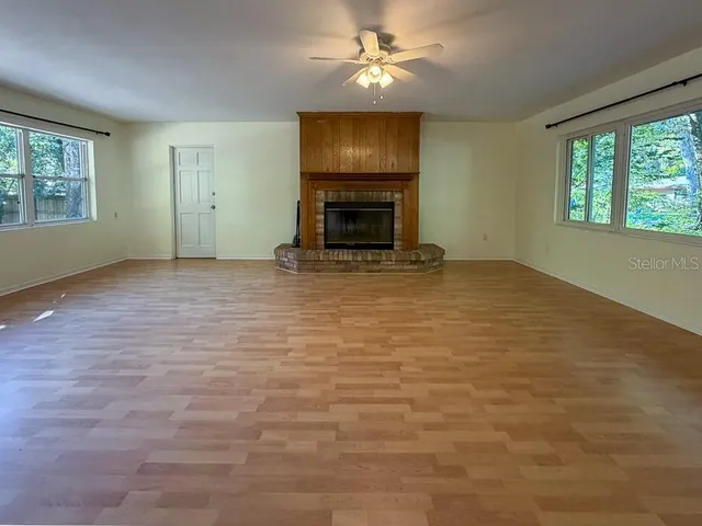 an empty room with windows fireplace and a ceiling fan