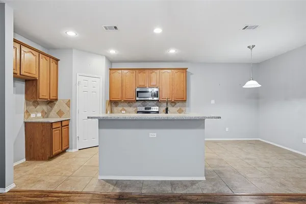 a large kitchen with granite countertop a stove a sink a refrigerator and white cabinets with wooden floor