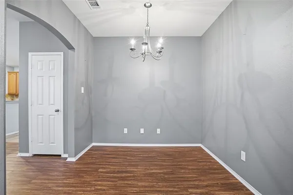 a view of an empty room with chandelier fan and wooden floor