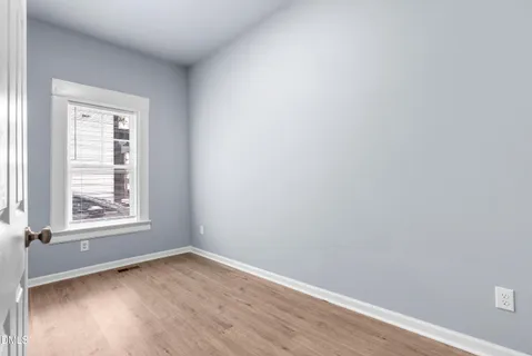 an empty room with wooden floor cabinet and windows