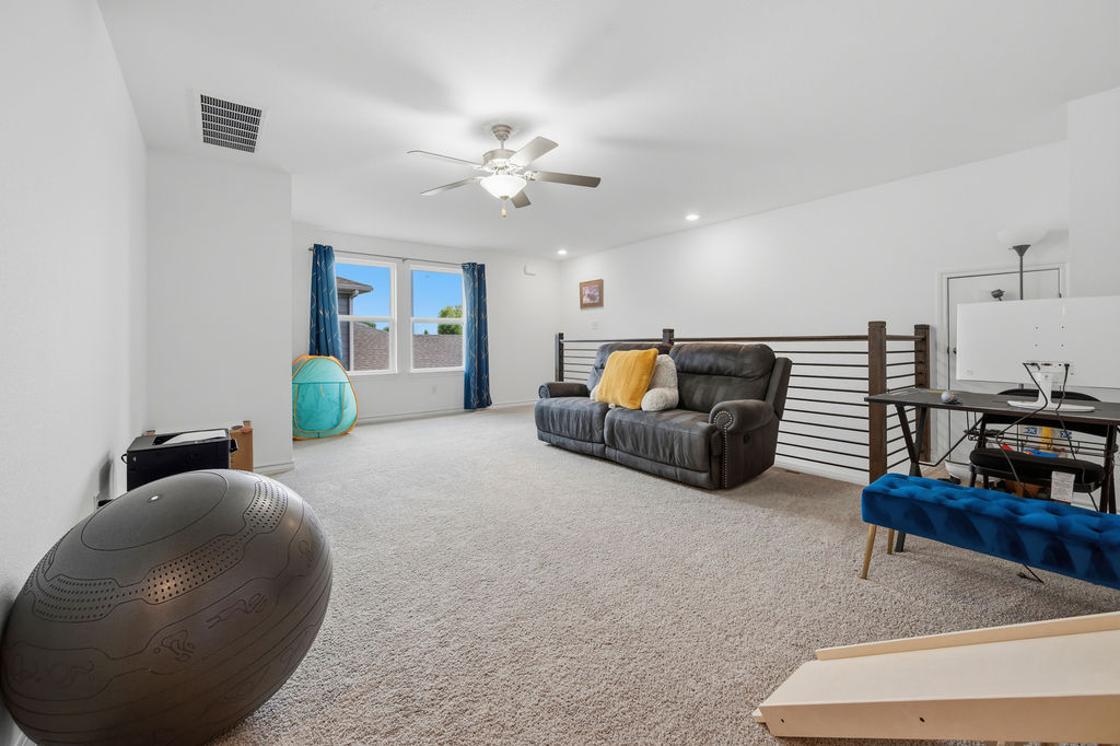 205 Stinchcomb Road Hutto, TX 78634 - Photo 27 of 29 An inviting open loft space features comfortable carpeting and ample natural light from several windows, ideal for relaxation or a home office.