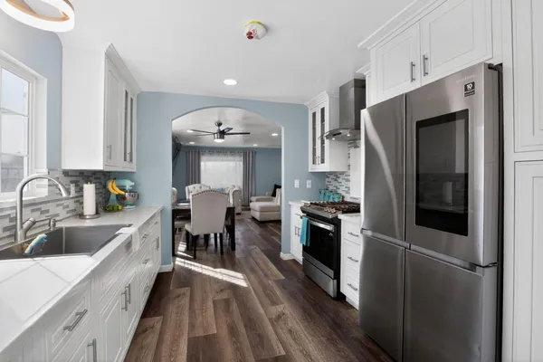 a kitchen with stainless steel appliances granite countertop a refrigerator a sink dishwasher a stove and white countertops with wooden floor