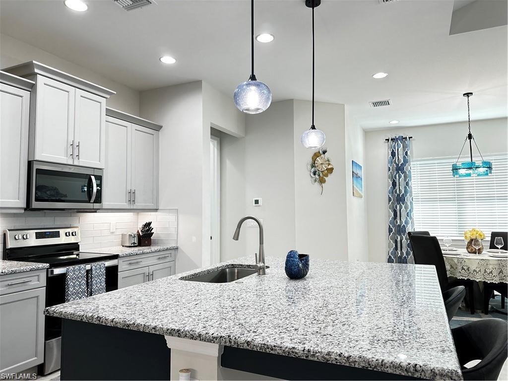 7135 Cayo Coco Lane Naples, FL 34113 - Photo 3 of 41 Kitchen with a breakfast bar, stainless steel appliances, light stone countertops, and a center island with sink