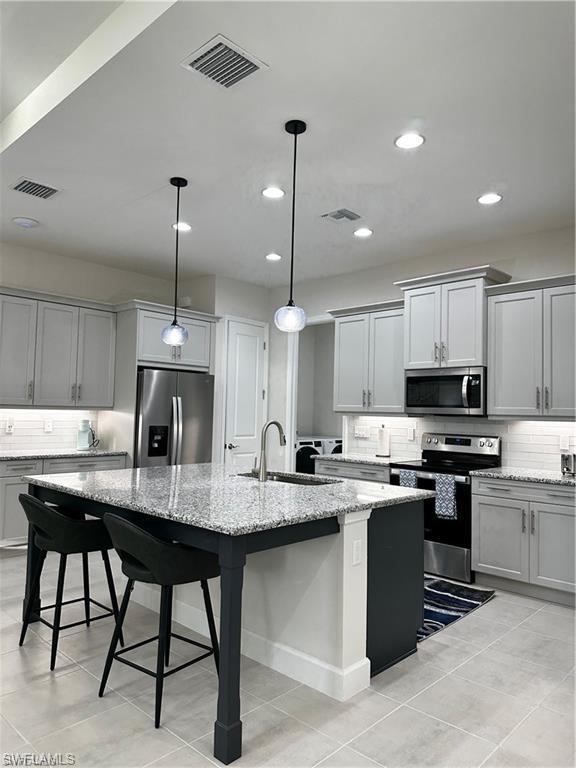 7135 Cayo Coco Lane Naples, FL 34113 - Photo 7 of 41 Kitchen featuring tasteful backsplash, stainless steel appliances, light stone counters, a center island with sink, and decorative light fixtures