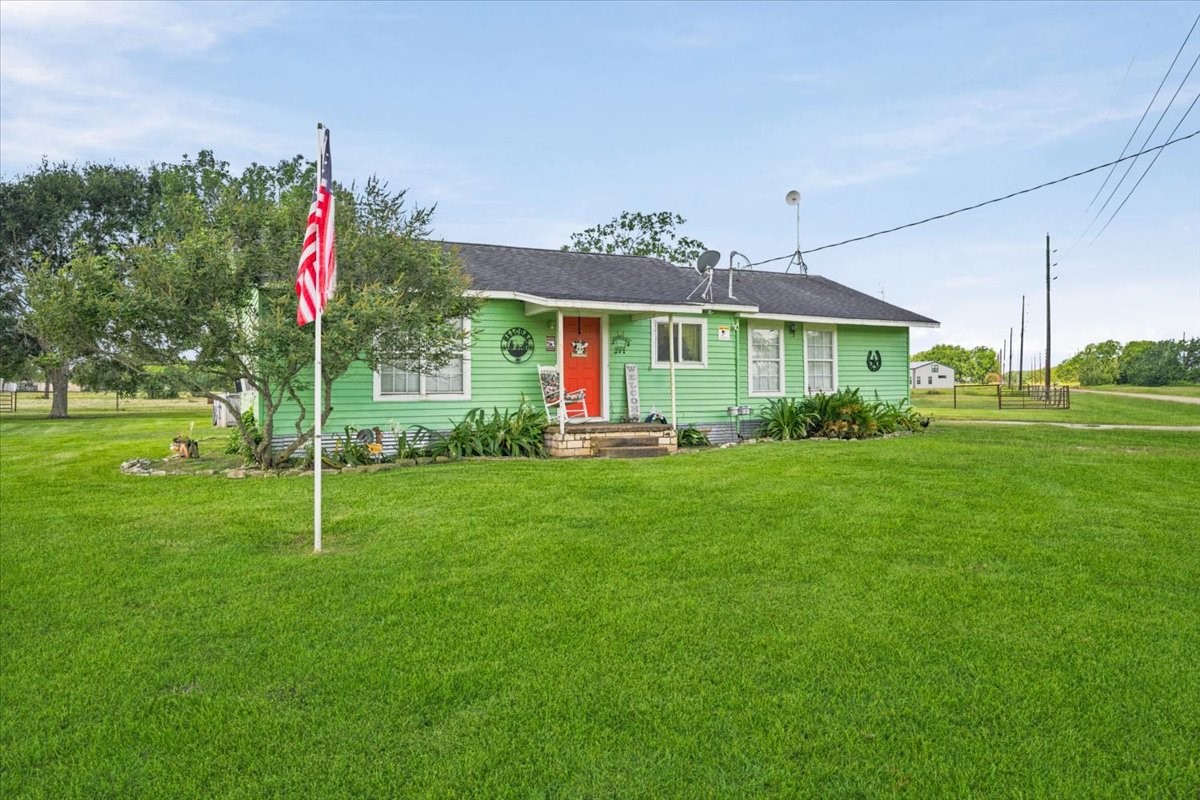 765 Norcross Road Wallis, TX 77485 - Photo 1 of 42 Charming single-story home with a welcoming red door, set on a spacious, well-maintained lawn. Features a cozy front porch, mature trees, and a flagpole, creating a picturesque and inviting atmosphere.