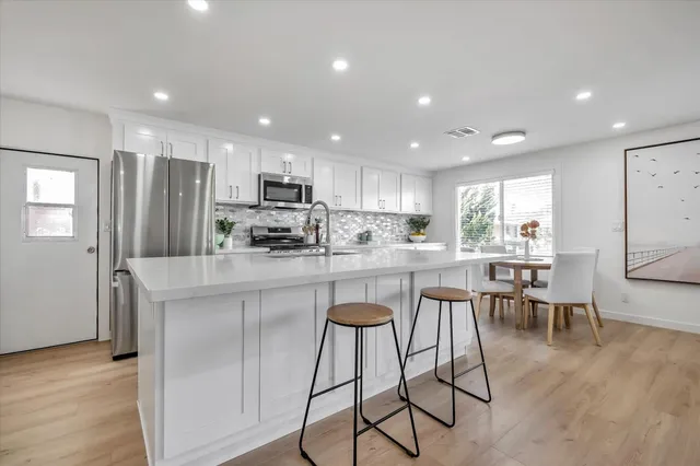 a kitchen with stainless steel appliances granite countertop a refrigerator a stove a sink a dining table and chairs with wooden floor