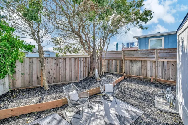 a backyard of a house with table and chairs wooden fence and trees