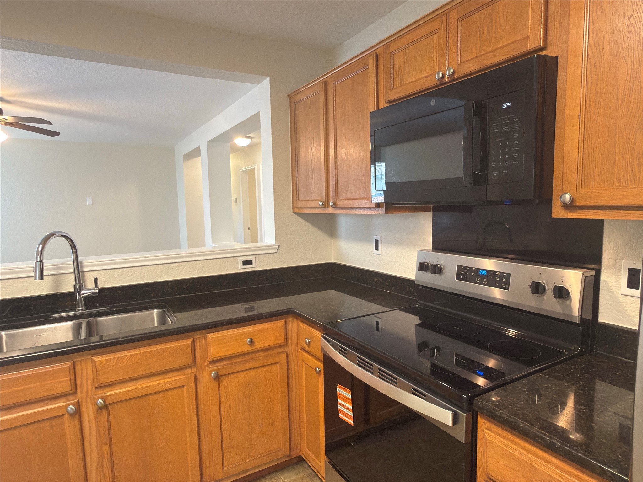 255 Myrtle Street Kyle, TX 78640 - Photo 6 of 31 Kitchen featuring wood cabinetry, dark countertops, stainless steel sink with gooseneck faucet, black over-the-range microwave, and stainless steel range