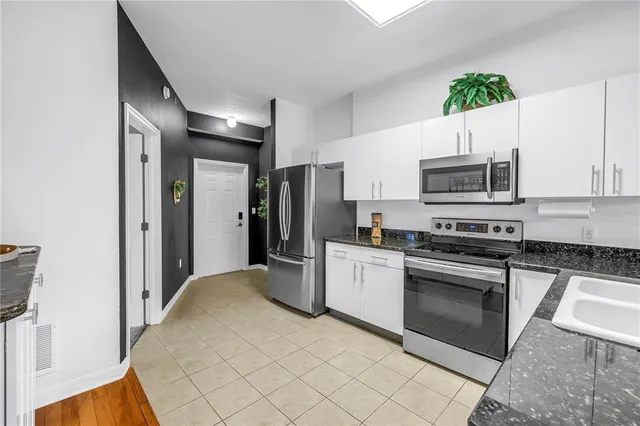 a kitchen with stainless steel appliances a stove a sink a refrigerator a microwave a sink and white cabinets