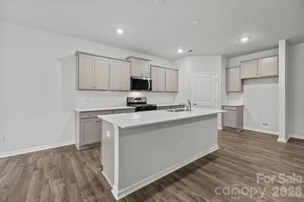 a kitchen with kitchen island white cabinets a sink a stove a microwave and wooden floors
