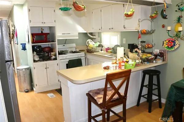 a kitchen with stainless steel appliances kitchen island granite countertop a refrigerator a stove a sink and white cabinets with wooden floor