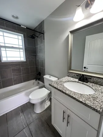 a bathroom with a granite countertop sink a toilet a mirror and bathtub
