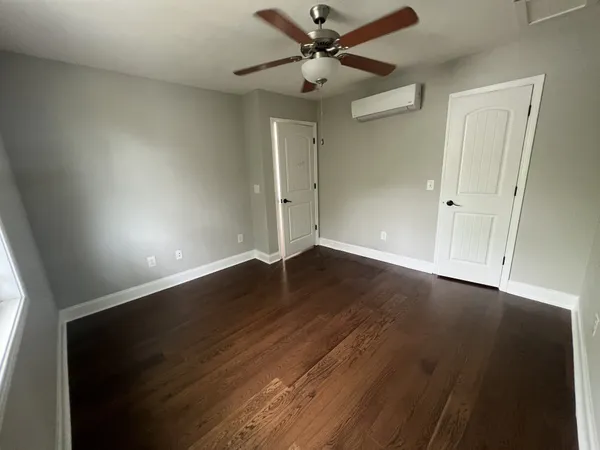 an empty room with wooden floor fan and windows