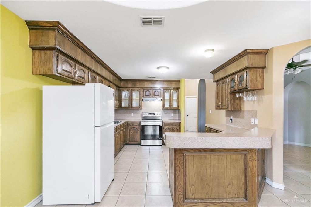 240 East Dicker Road Pharr, TX 78577 - Photo 7 of 23 Kitchen featuring wood-finish cabinetry, tile flooring, and a built-in breakfast bar with a stone-finish countertop