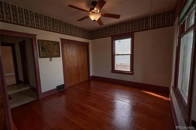 an empty room with wooden floor chandelier fan and windows