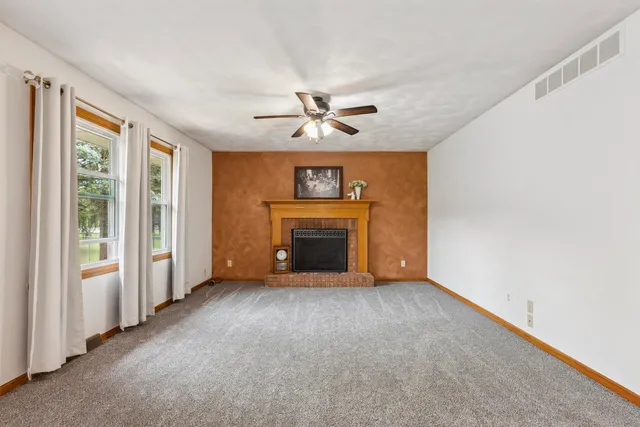 an empty room with windows chandelier fan and a fireplace
