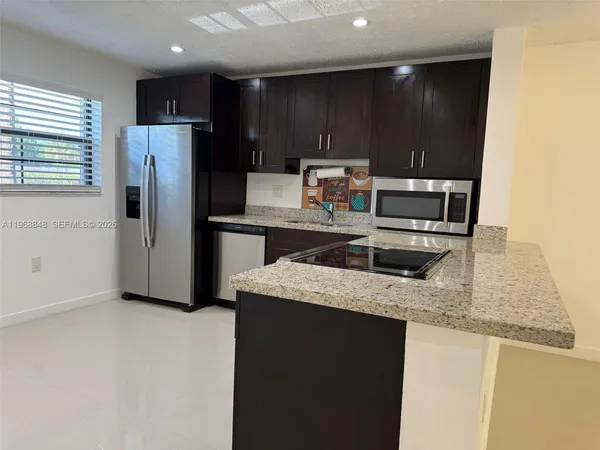 a kitchen with stainless steel appliances granite countertop a refrigerator a stove and a sink with wooden cabinets