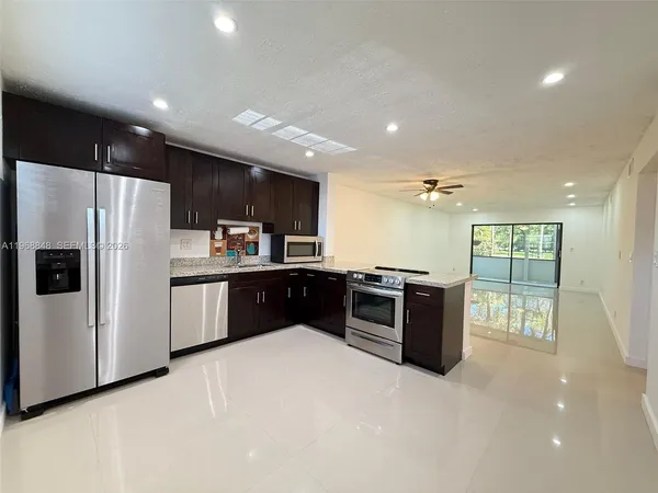 a kitchen with stainless steel appliances kitchen island granite countertop a refrigerator a sink a stove top oven and a refrigerator with wooden floor