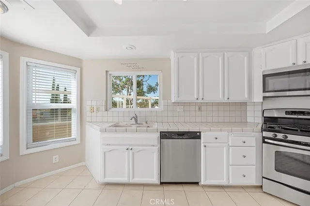 a kitchen with white cabinets appliances a sink and a window