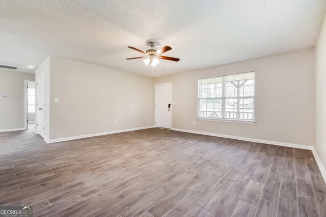 an empty room with wooden floor ceiling fan and windows