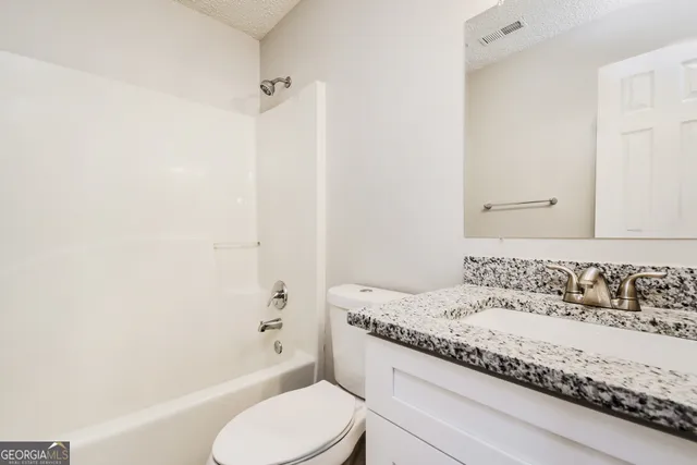 a bathroom with a granite countertop bathtub shower sink vanity and toilet
