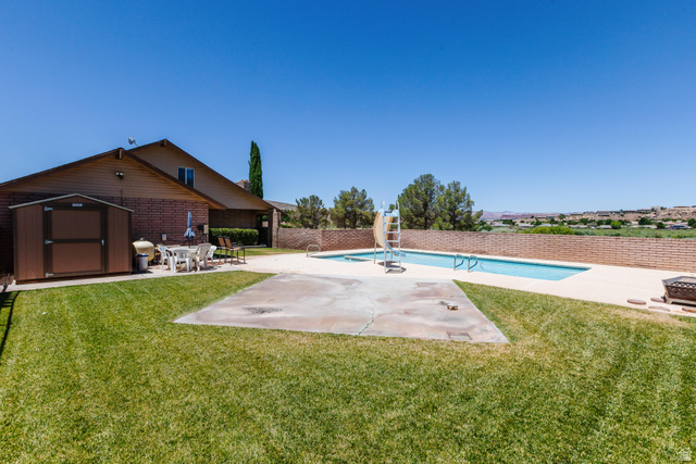 1470 Redwood Tree Street St. George, UT 84790 - Photo 50 of 53 Expansive backyard featuring a rectangular swimming pool with surrounding concrete decking, a brick privacy wall, a brown storage shed, and a dedicated patio area
