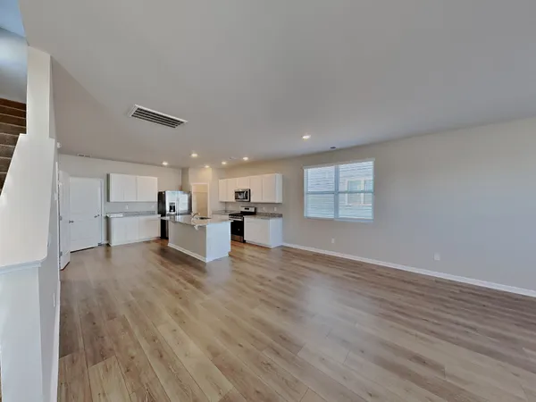 a view of empty room with wooden floor and kitchen