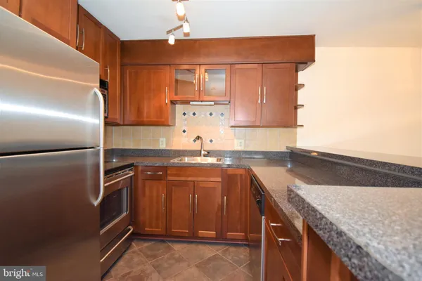 a kitchen with granite countertop a refrigerator a stove and a sink with wooden floor
