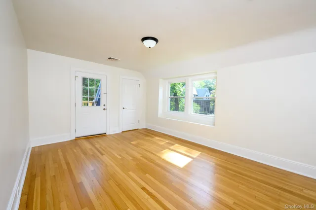 a view of an empty room with wooden floor and a window