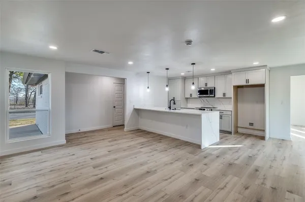 a large white kitchen with kitchen island a sink dishwasher a refrigerator and white cabinets with wooden floor