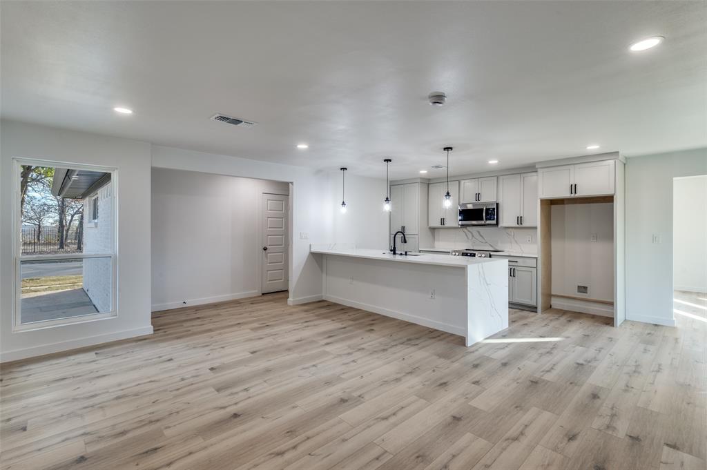 116 Cooper Drive Hurst, TX 76053 - Photo 6 of 25 a large white kitchen with kitchen island a sink dishwasher a refrigerator and white cabinets with wooden floor